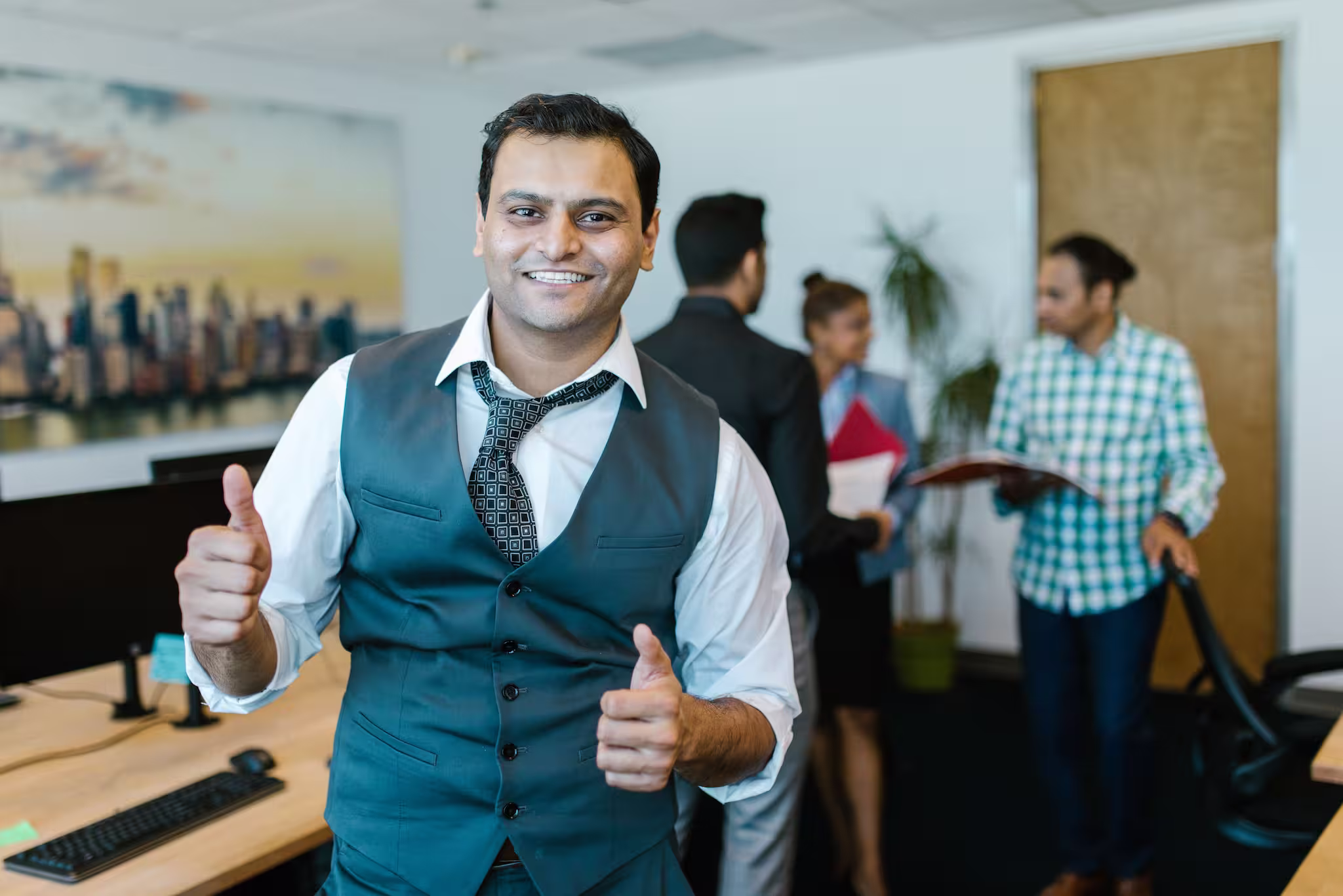 Smiling professional showing thumbs up in a lively Visa consultation office environment with colleagues in the background